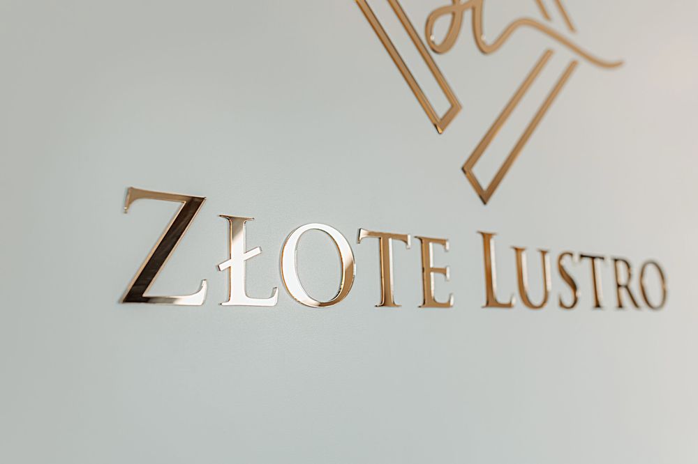 Złocony szyld z logo gabinetu kosmetycznego Złote Lustro na ścianie